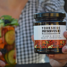 Load image into Gallery viewer, Person holding a jar of Yorkshire Preserves Pimm's Mixed Berry Conserve with a blurred background