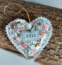 Load image into Gallery viewer, Floral heart-shaped fabric ornament with 'HUGS' label on a wooden surface
