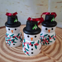 Load image into Gallery viewer, Three small hand-painted snowman ornaments with black hats, red ribbons, and green holly accents, displayed on a circular wood slice background.
