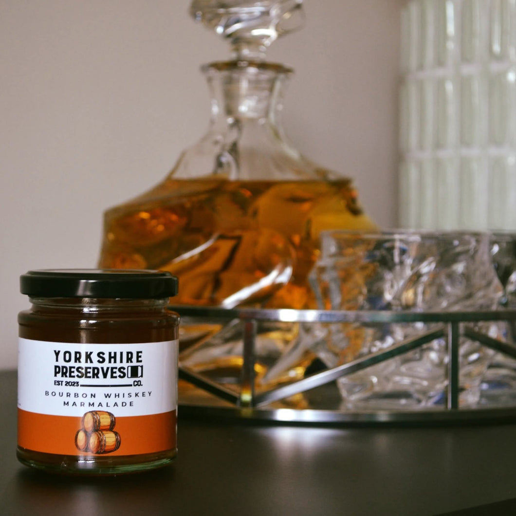Jar of Yorkshire Preserves' bourbon whiskey marmalade with a decanter and glass in the background.