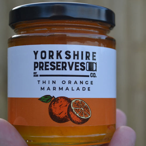 Jar of Yorkshire Preserves thin orange marmalade held in hand with a blurred background