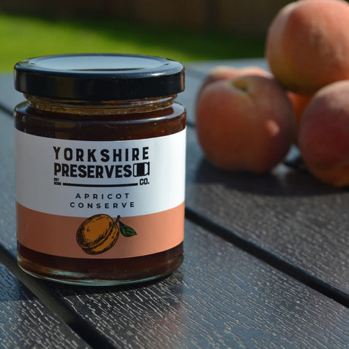 Jar of Yorkshire Preserves apricot conserve on a wooden table with apricots.