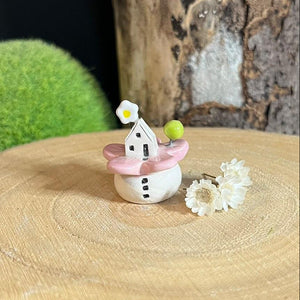 Small decorative item resembling a fairy house with pink roof on a wooden surface.