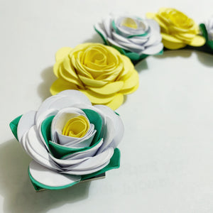 Decorative wreath made of yellow, white, and green paper flowers on a white background