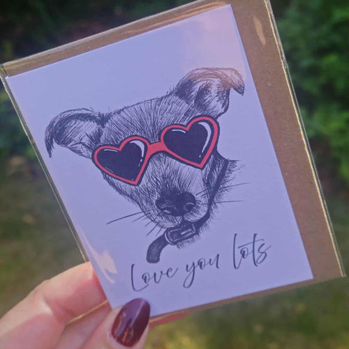 Card with a dog illustration wearing heart sunglasses and 'Love you lots' text, held by a hand.